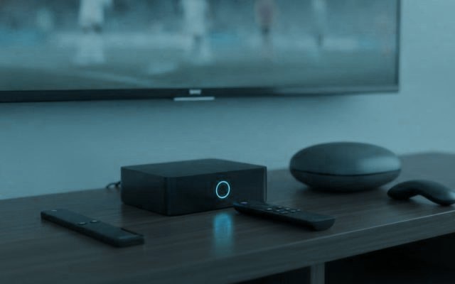 A streaming stick, a set-top box and a round streaming box with their remotes on a TV console