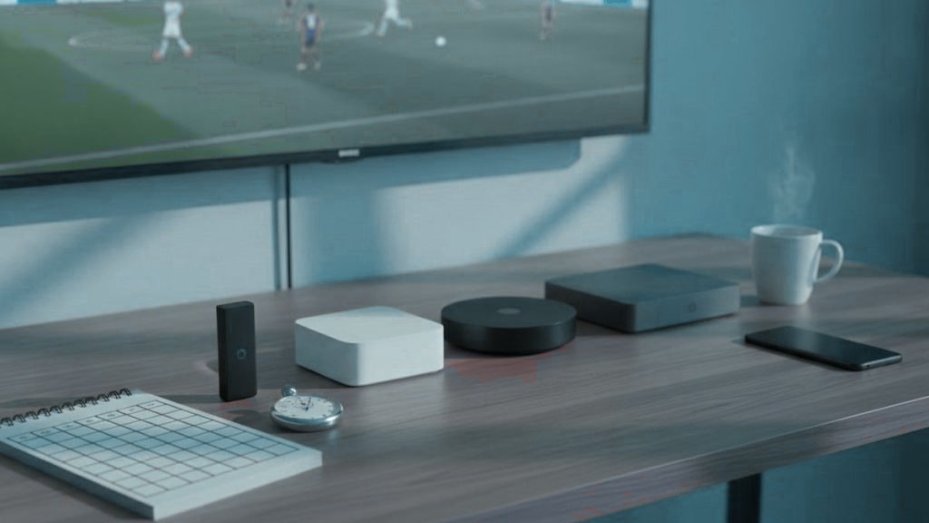 Five streaming devices, a notebook scoring grid and a stopwatch in front of a TV showing a football match